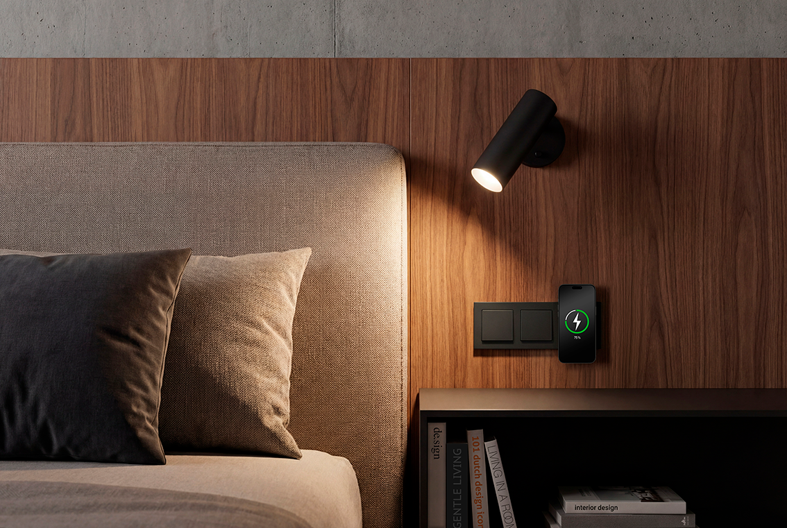 JUNG Magnetic Charger naast het bed met draadloos opladende smartphone in zwart schakelmateriaal